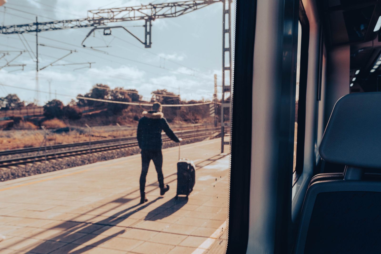 Traveler with a wheeled suitcase on a platform, seen from a train